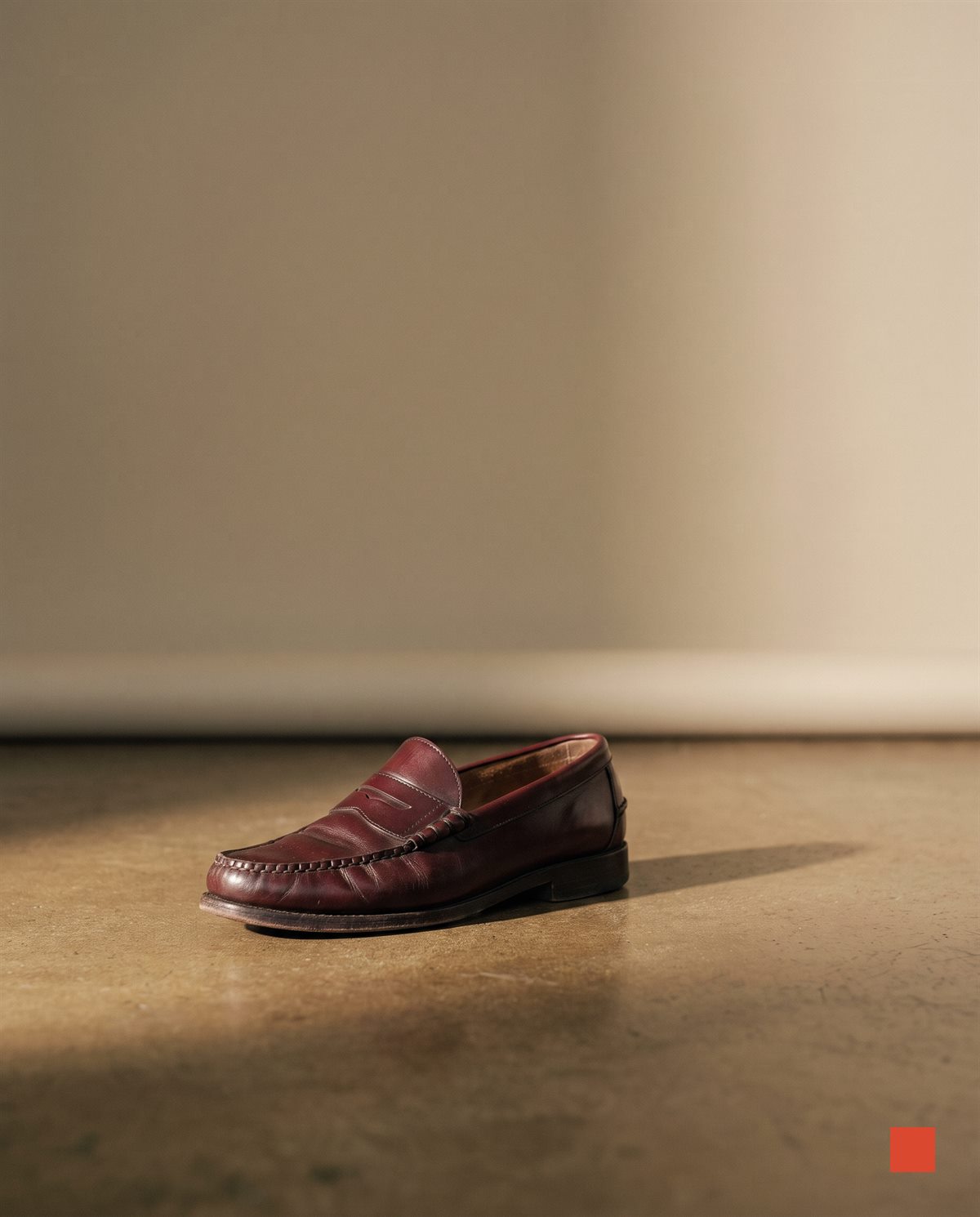 Burgundy penny loafer on a concrete floor with a long shadow